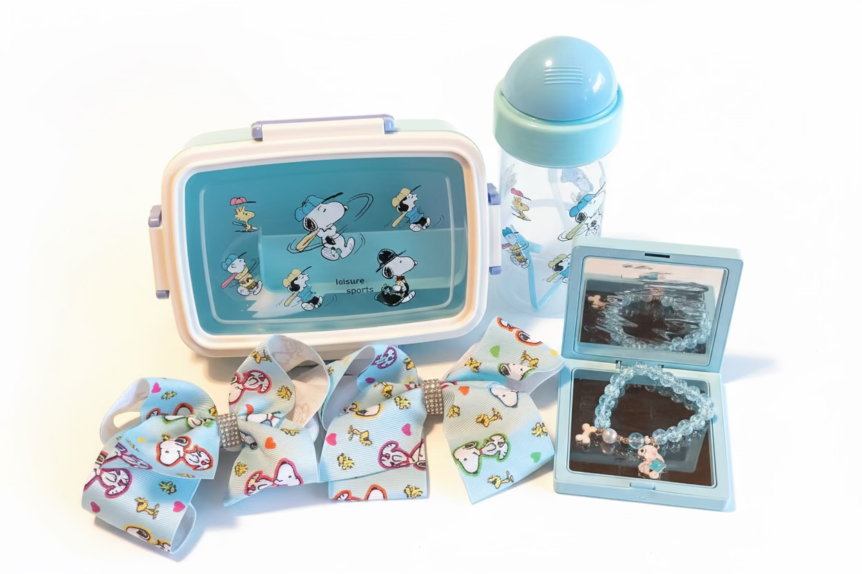 A collection of Peanuts-themed items, including a lunchbox, a water bottle, two hair bows, and a beaded bracelet in a small case.