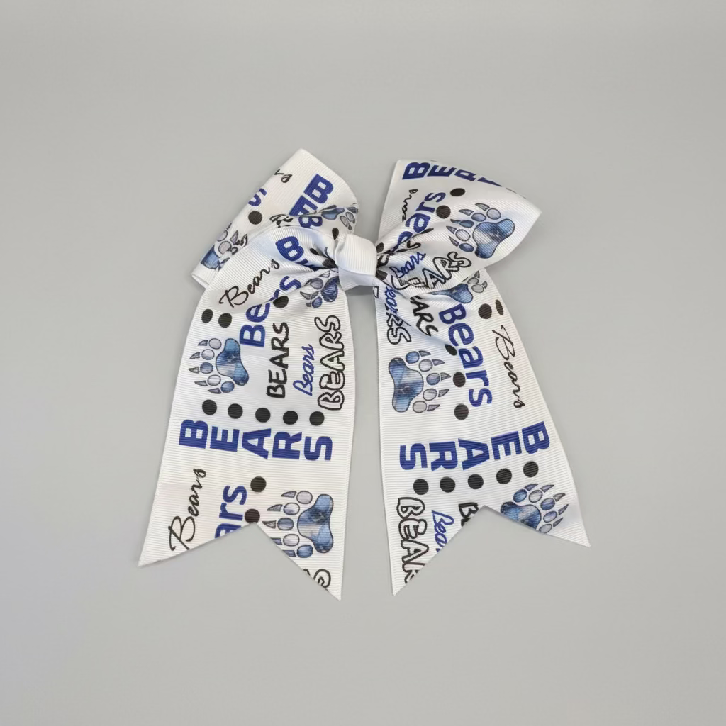 A white grosgrain ribbon hair bow featuring blue paw prints, black polka dots, and 'BEARS' text printed all over, displayed on a white faux fur background.