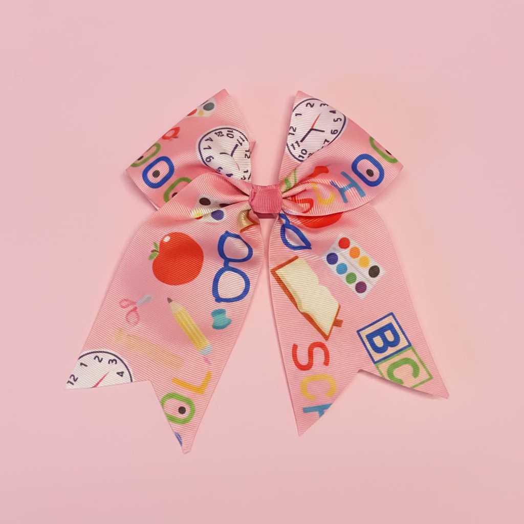 A pink grosgrain ribbon hair bow decorated with school-themed illustrations including books, pencils, apples, glasses, and colorful letters, displayed on a white faux fur background.
