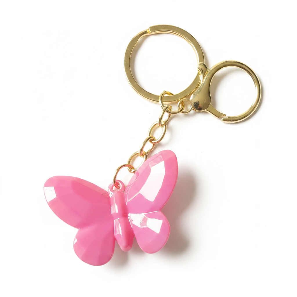 A pink glossy butterfly-shaped keychain with gold-tone metal rings and chain, shown on a black textured surface.