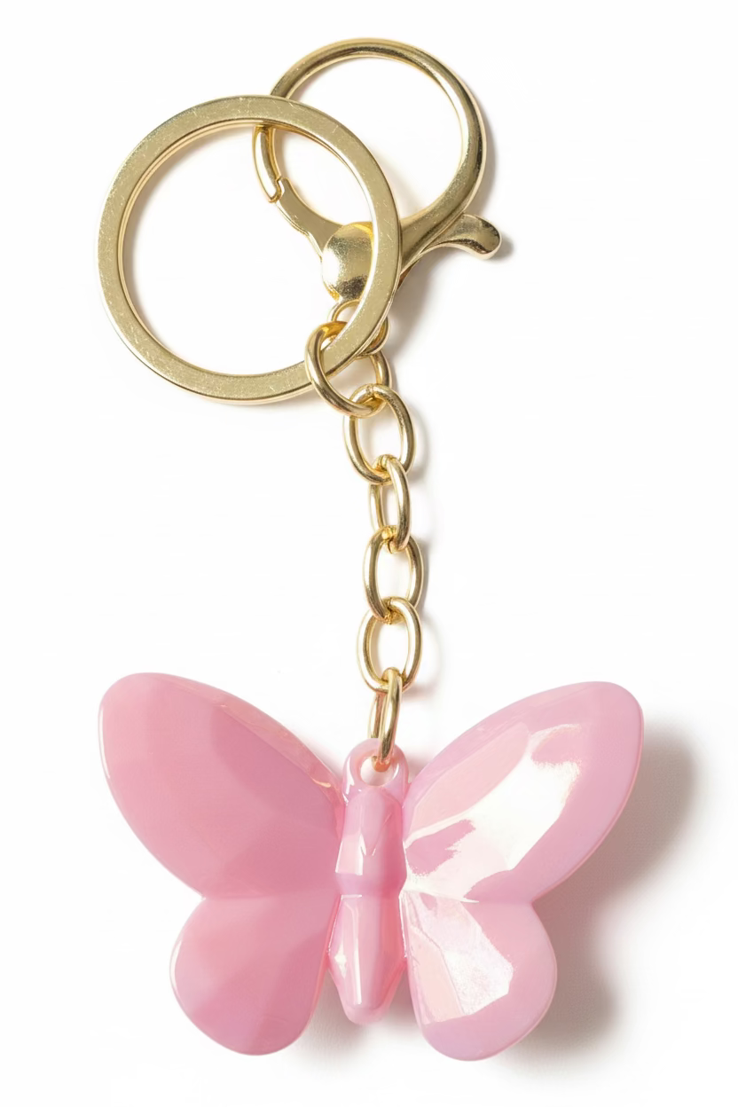 A pink butterfly-shaped keychain with iridescent wings and gold-tone metal rings and chain, shown on a black textured surface.