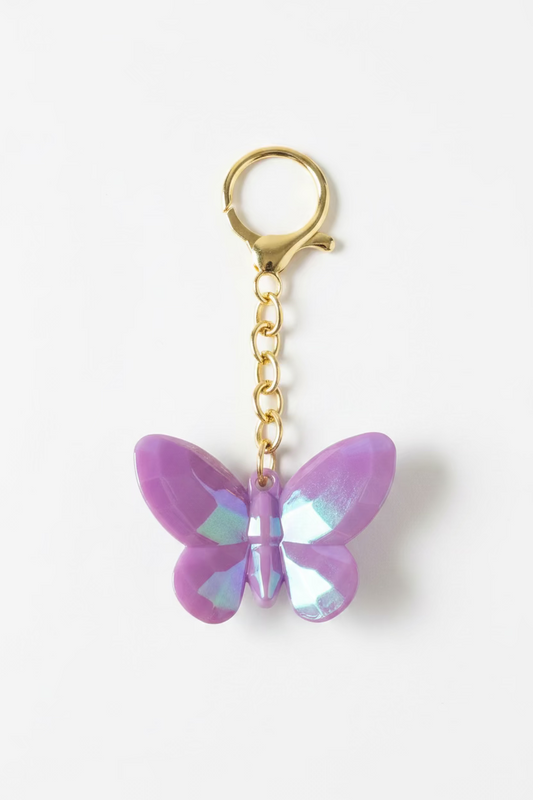 A butterfly-shaped keychain with iridescent lavender-purple wings and gold-tone metal hardware, shown on a black textured surface.