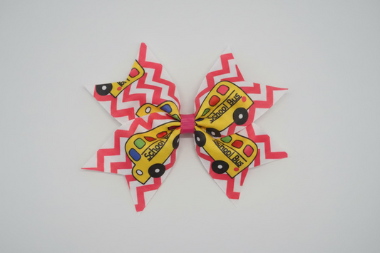 A large hair bow featuring a pink and white chevron pattern with yellow school bus illustrations, displayed on a white faux fur background.